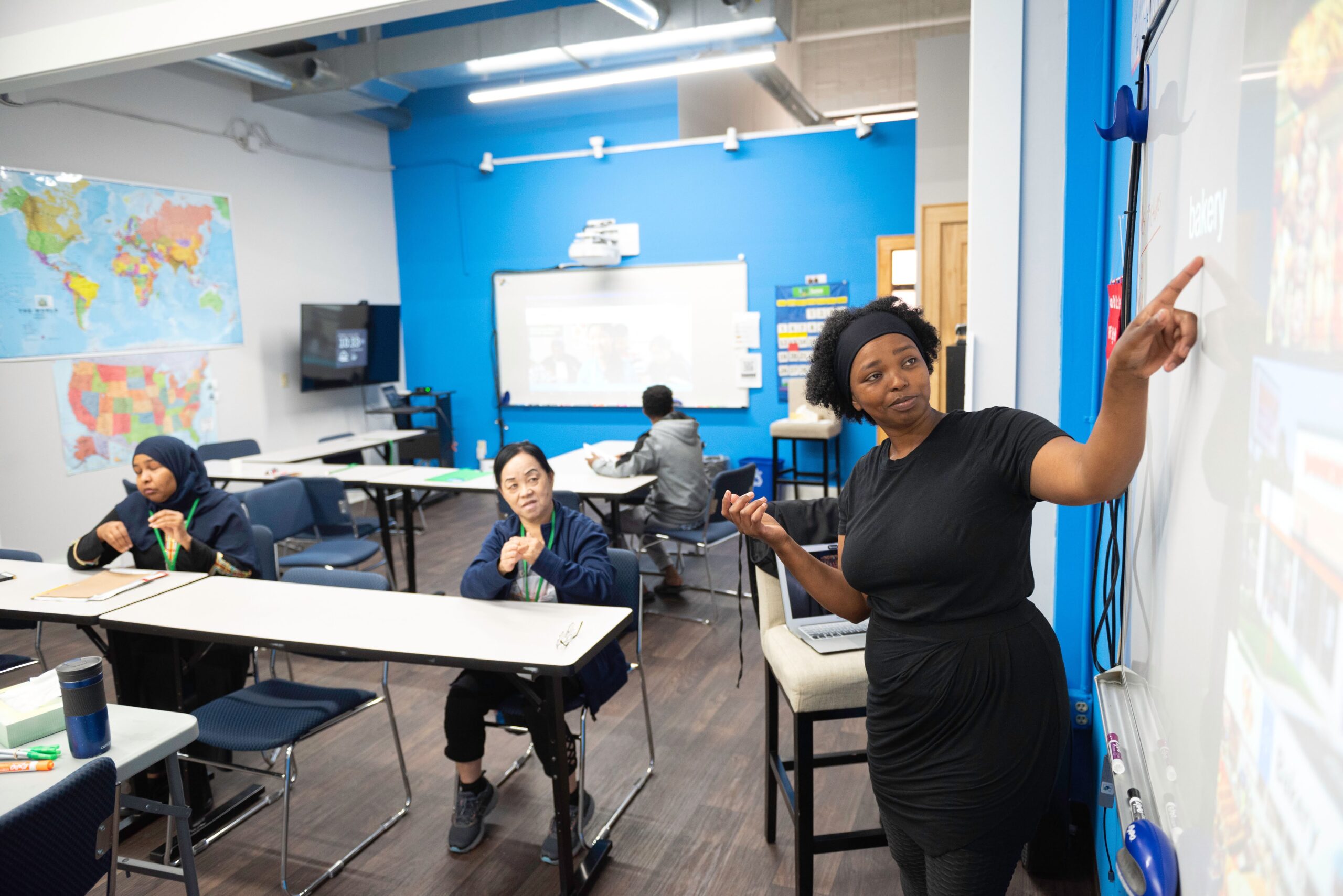 A teacher points to the whiteboard in front of a class